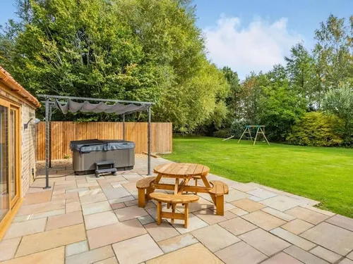 Cottage patio with wooden picnic table and hot tub facing large lawn with swings.