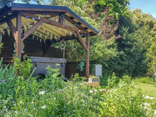 Wooden garden gazebo with hot tub beside a cottage, surrounded by greenery and flowers