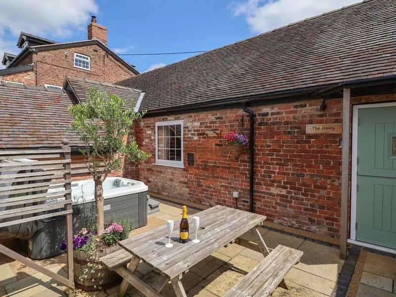 The Dairy brick exterior with outdoor hot tub, picnic table and drinks on patio.