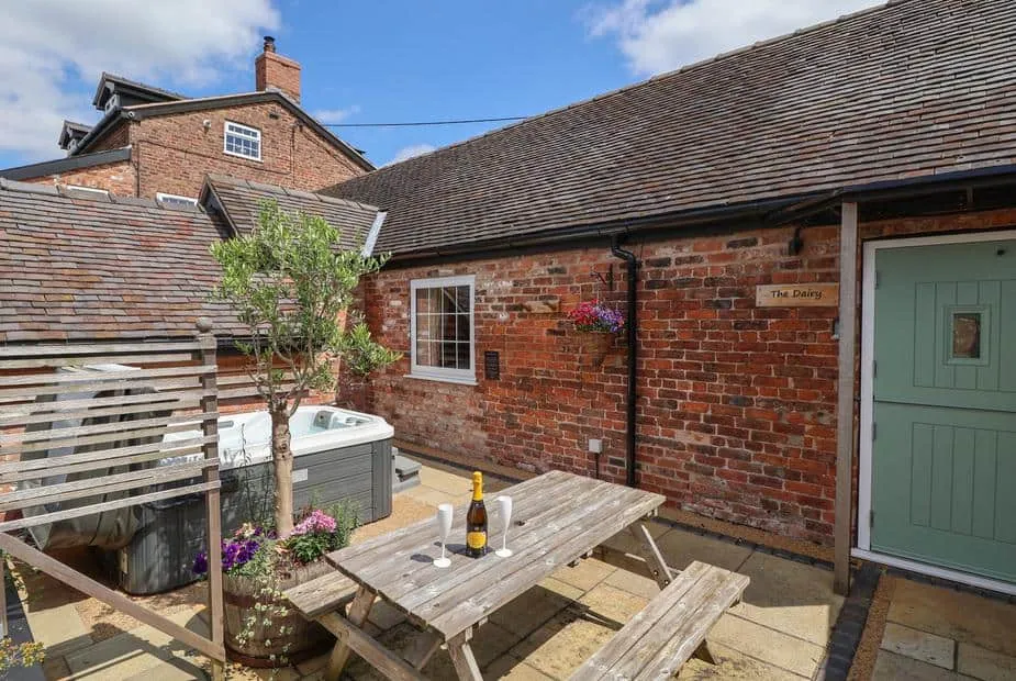 The Dairy brick exterior with outdoor hot tub, picnic table and drinks on patio.