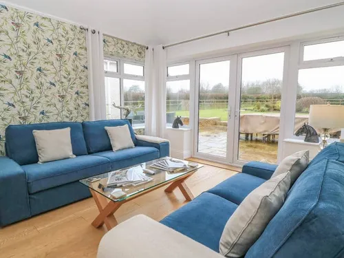 Cottage lounge with blue sofas and glass coffee table by patio doors