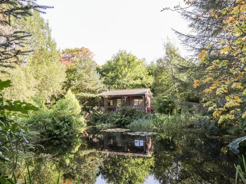 The Log Cabin surrounded by trees with a pond in the foreground.
