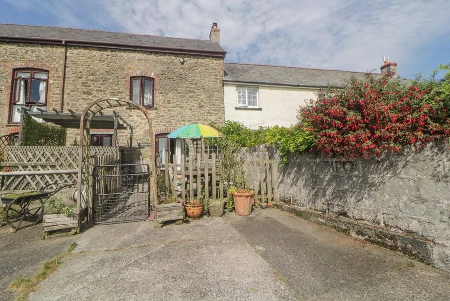 Stone-walled The Orchard cottage with patio, wooden gate and colourful umbrella.