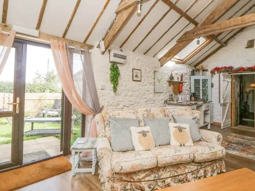Cottage lounge with floral sofa and exposed beams, doors opening to garden