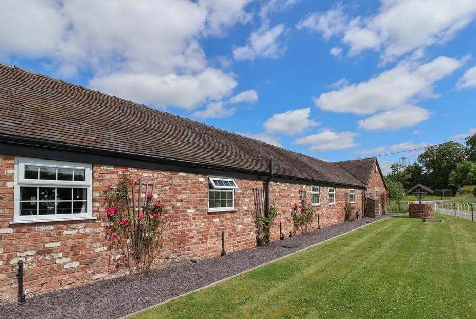 Long brick exterior of The Shippon with lawn and a well in the garden.