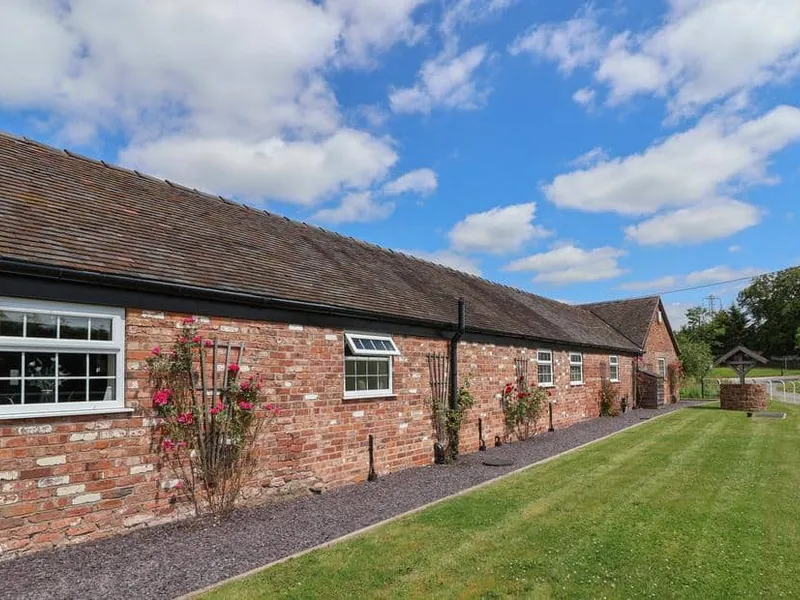 Long brick exterior of The Shippon with lawn and a well in the garden.