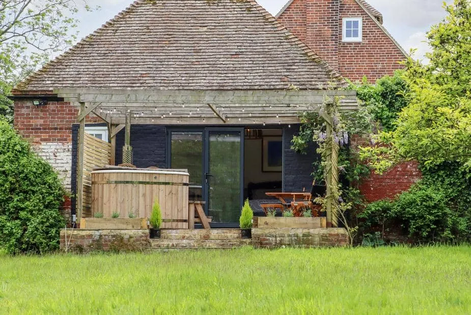 The Snug exterior with wooden hot tub and pergola in garden.
