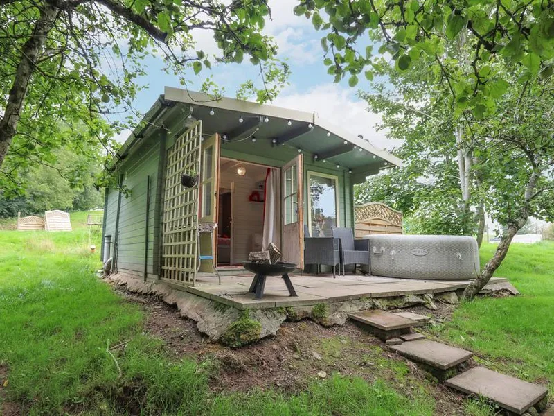 Ty Bach Twt lodge with outdoor hot tub and deck set in a grassy woodland clearing