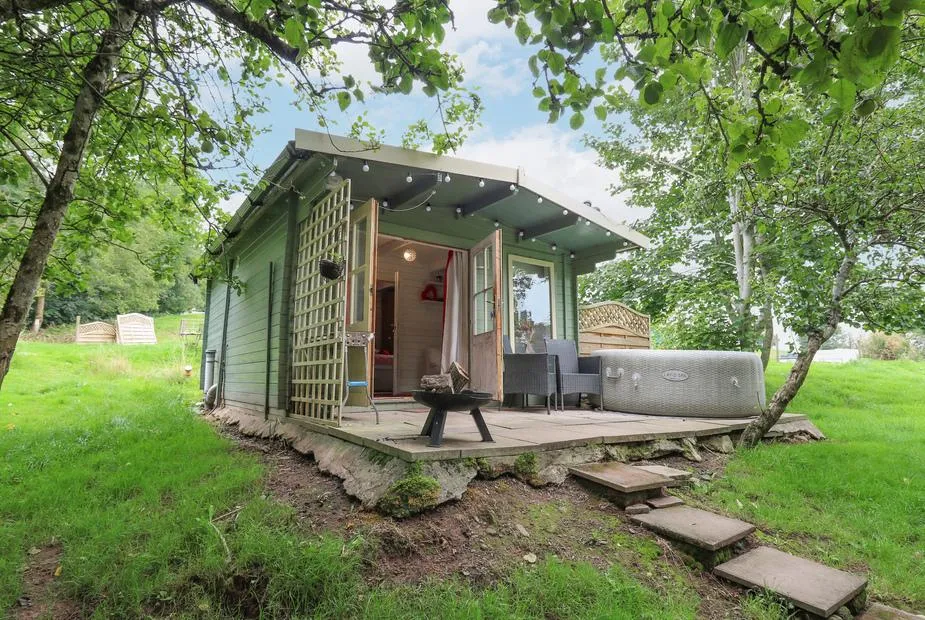 Ty Bach Twt lodge with outdoor hot tub and deck set in a grassy woodland clearing