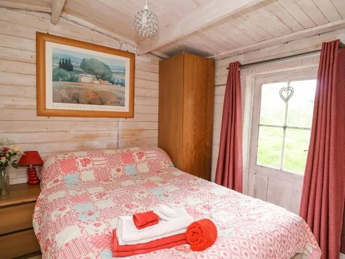 Lodge bedroom with double bed, bedside tables, wardrobe and door with red curtains