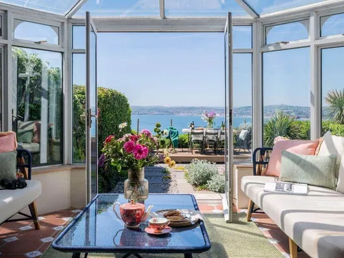 Conservatory in cottage with sea view and patio dining table visible through open doors