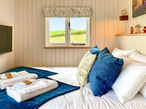 Lodge bedroom with double bed, blue cushions, window view, and TV on the wall