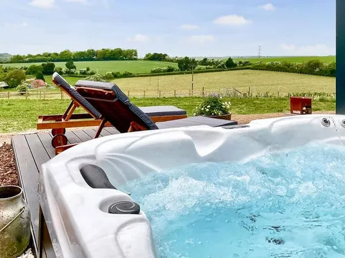 Lodge deck with hot tub and sun loungers overlooking fields