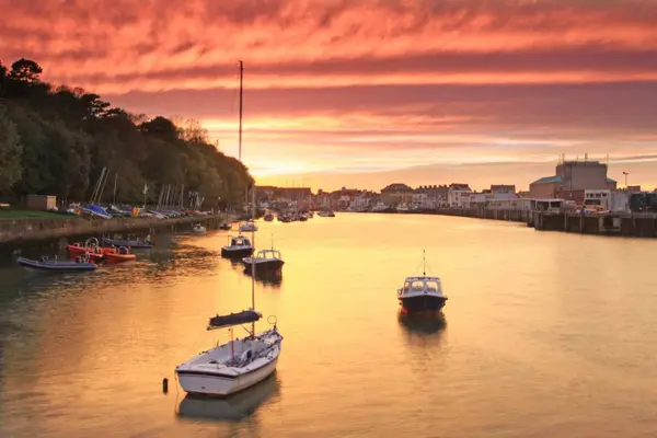 Sunset over the historic Weymouth Harbour, featuring moored boats and the townscape bathed in warm evening light.