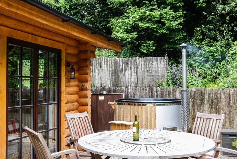 Wilderness Lodge wooden deck with round table and outdoor hot tub in leafy garden setting.