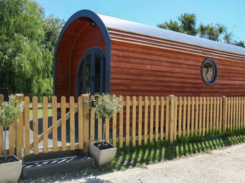 Willow Pod arched timber cabin with picket fence and potted plants at entrance