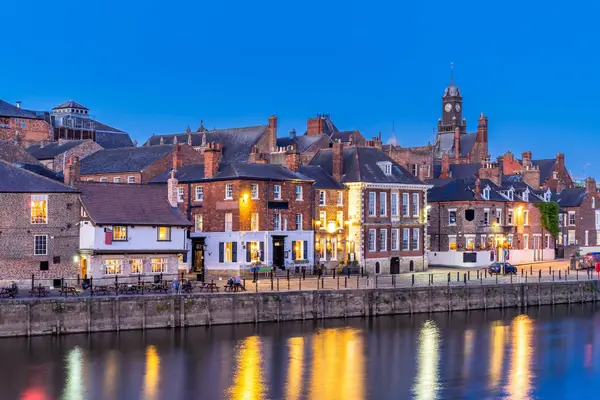 Warm lights from riverside pubs reflecting in the River Ouse in York at dusk